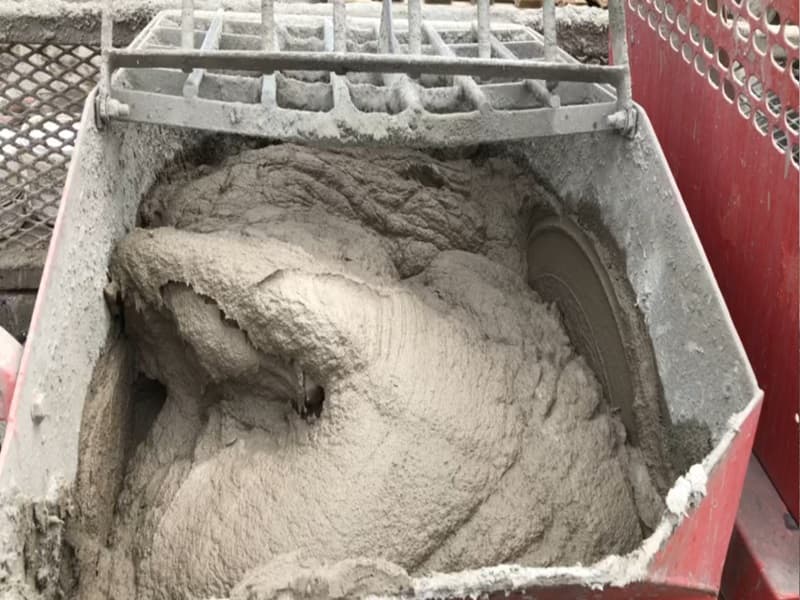 A close-up view of freshly mixed parging mortar inside a red mixing machine, showing its thick, smooth consistency.